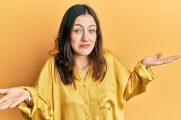 Young brunette woman wearing casual yellow shirt clueless and confused expression with arms and...