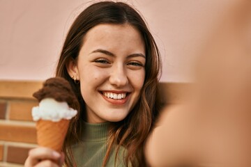 Young caucasian girl eating ice cream making selfie by the camera at the city.