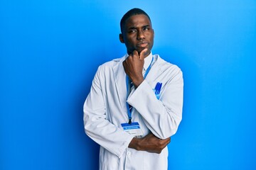 Young african american man wearing scientist uniform serious face thinking about question with hand on chin, thoughtful about confusing idea