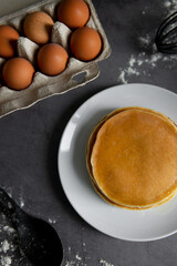 baking cupcakes composition. eggs, cupcakes, flour, milk, whisk and spoon on a dark background. Close up of baked pancakes on a white plate.