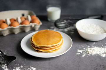baking cupcakes composition. eggs, cupcakes, flour, milk, whisk and spoon on a dark background. Close up of baked pancakes on a white plate.