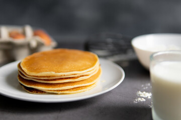 baking cupcakes composition. eggs, cupcakes, flour, milk, whisk and spoon on a dark background. Close up of baked pancakes on a white plate.