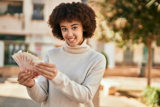 Young hispanic girl smiling happy holding israel shekels at the city.