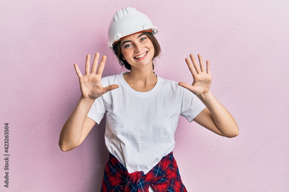 Sticker Young caucasian woman wearing hardhat showing and pointing up with fingers number ten while smiling confident and happy.