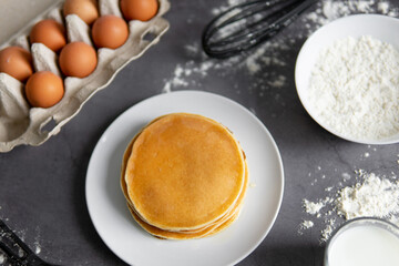 baking cupcakes composition. eggs, cupcakes, flour, milk, whisk and spoon on a dark background. Close up of baked pancakes on a white plate.