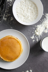 baking cupcakes composition. eggs, cupcakes, flour, milk, whisk and spoon on a dark background. Close up of baked pancakes on a white plate.