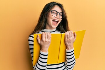 Young caucasian woman reading a book wearing glasses smiling and laughing hard out loud because...