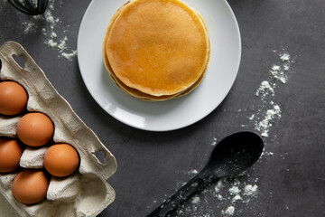 baking cupcakes composition. eggs, cupcakes, flour, milk, whisk and spoon on a dark background. Close up of baked pancakes on a white plate.