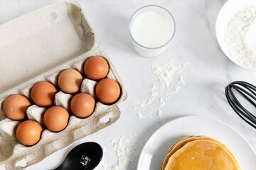 composition of small desserts for baking. eggs, muffins, flour, milk, whisk and spoon on a light background. Close-up of baked pancakes on a white plate.