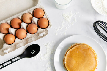 composition of small desserts for baking. eggs, muffins, flour, milk, whisk and spoon on a light background. Close-up of baked pancakes on a white plate.
