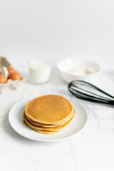 composition of small desserts for baking. eggs, muffins, flour, milk, whisk and spoon on a light background. Close-up of baked pancakes on a white plate.