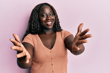 African young woman wearing casual clothes looking at the camera smiling with open arms for hug. cheerful expression embracing happiness.