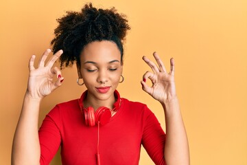 Young african american girl listening to music using headphones relax and smiling with eyes closed doing meditation gesture with fingers. yoga concept.