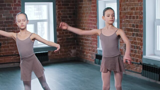 Two ballerina girls train synchronized movements in the studio