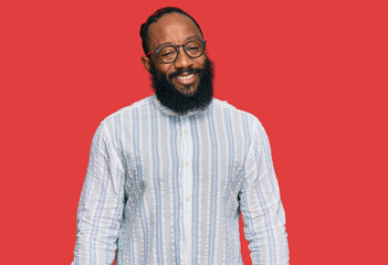 Obraz premium Young african american man wearing business shirt and glasses looking positive and happy standing and smiling with a confident smile showing teeth