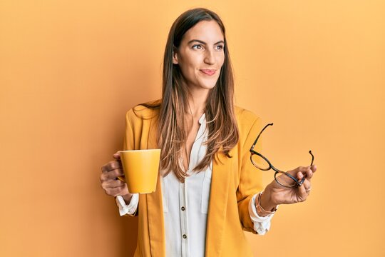 Young beautiful woman wearing business style drinking cup of coffee smiling looking to the side and staring away thinking.