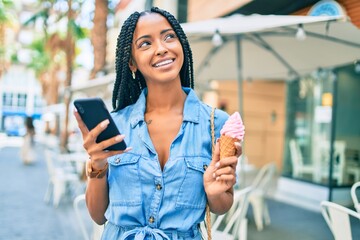 Young african american woman using smartphone and eating ice cream at the city.