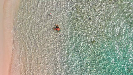 Young girl enjoying a beautiful beach shoreline. Crystal clear ocean water, downward view from drone