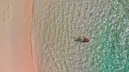 Young girl enjoying a beautiful beach shoreline. Crystal clear ocean water, downward view from drone