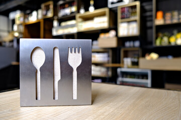 Cutlery symbols cut out on a metal holder for paper napkins on a wooden table in a small gourmet shop interior.