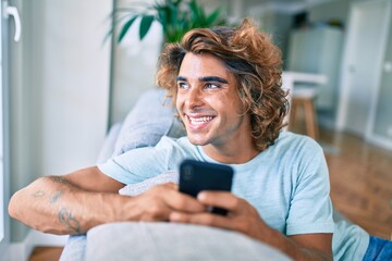 Young hispanic man smiling happy using smartphone at home