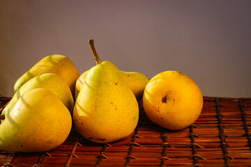 Several ripe yellow pears stand on a wicker basket illuminated by rays of the sun