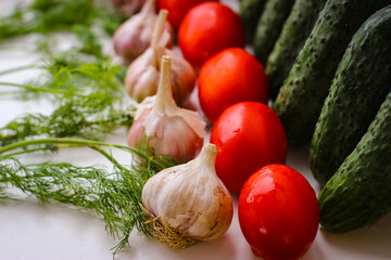 Several green cucumbers and red tomatoes and garlic  are stay in a rows on a white background