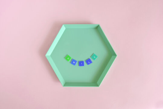 Naklejki SMILE - word made from colored letters on green hexagon plate on pink background. Top view. Copy space. Selective focus.