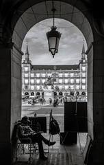 Black and white photograph of a man with a canvas painting in Plaza Mayor, Madrid.