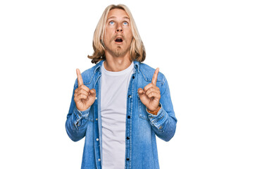 Obraz premium Caucasian man with blond long hair wearing casual denim jacket amazed and surprised looking up and pointing with fingers and raised arms.