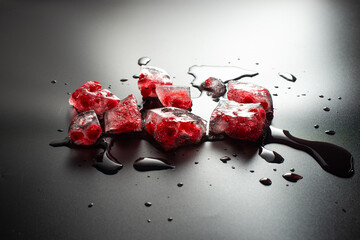 Red currant berries frozen in a piece of broken ice on a black background. Close-up of melting ice...