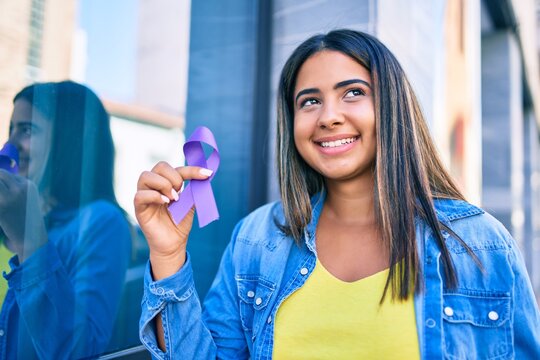 Young latin woman smiling happy holding purple ribbon at city.