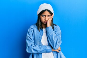 Young latin woman wearing cute wool cap thinking looking tired and bored with depression problems with crossed arms.