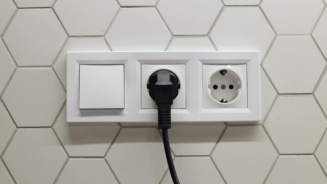 Man hand inserts a plug into black electrical outlet on white wall. Earth Hour saving electrical energy