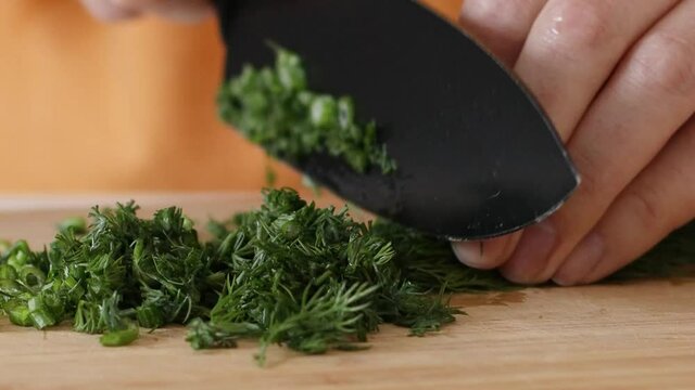Cut fresh green bunch of dill with a knife on a wooden board. Harvesting concept