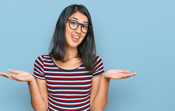 Beautiful asian young woman wearing casual clothes and glasses clueless and confused expression with arms and hands raised. doubt concept.