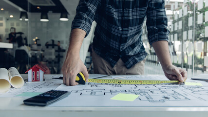 Architectural building design and construction plans with blueprints, Young man was designing a building or architecture with a ruler, pen, pencil, tape measure, architect hat and other equipment.