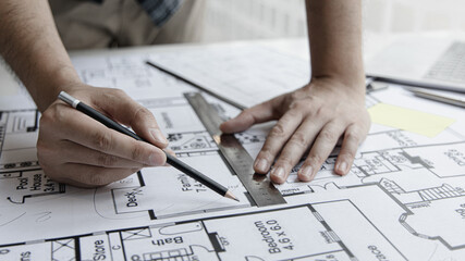 Architectural building design and construction plans with blueprints, Young man was designing a building or architecture with a ruler, pen, pencil, tape measure, architect hat and other equipment.