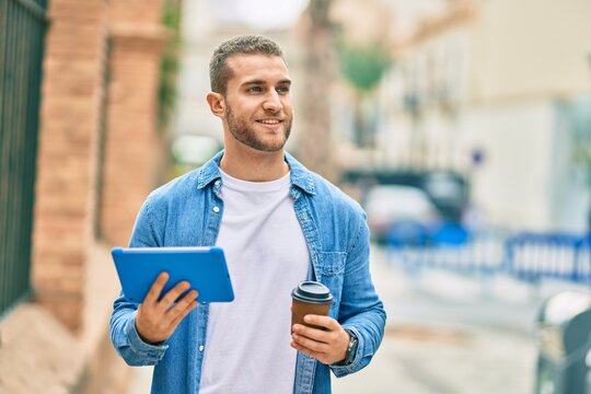 Young caucasian man smiling happy using touchpad and drinking coffee at the city.