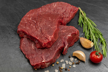 Fresh raw beef for steaks with spices on a black slate board.
