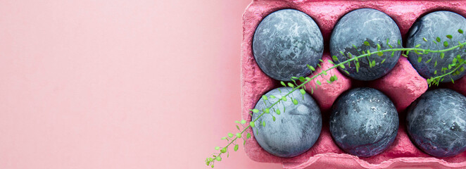 blue marble chicken eggs painted for easter in a pink box for eggs, green twig, place for text, top view happy easter concept, horizontal banner