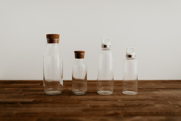 Four different size of eco friendly water bottles on wooden table with white background. Glass water bottles. Zero waste, sustainable solution to avoid using plastic. 