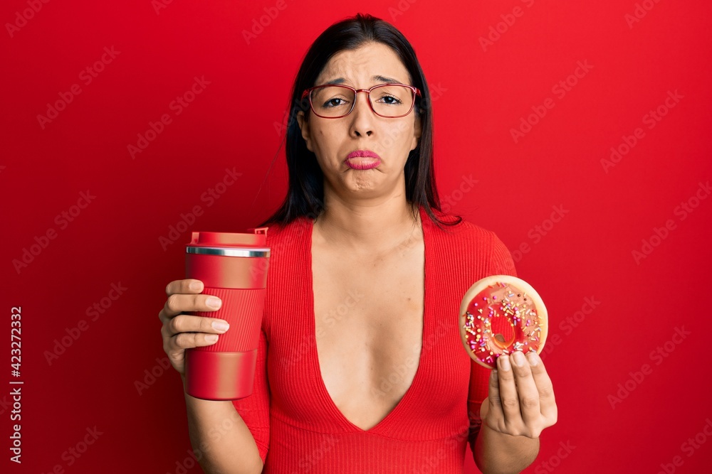 Poster young latin woman eating doughnut and drinking coffee depressed and worry for distress, crying angry