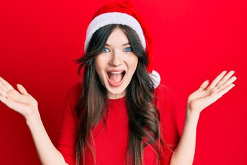 Young beautiful caucasian girl wearing christmas hat celebrating victory with happy smile and winner expression with raised hands