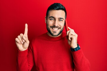 Fototapeta premium Young hispanic man having conversation talking on the smartphone smiling with an idea or question pointing finger with happy face, number one