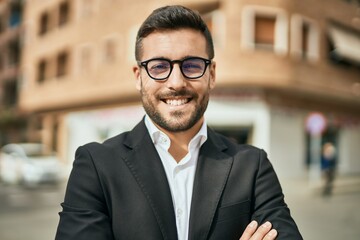 Fototapeta premium Young hispanic businessman with arms crossed smiling happy at the city.