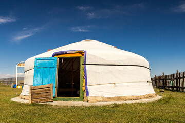Beautiful traditional Mongolian white Yurt with blue door, on green grass and very blue sky