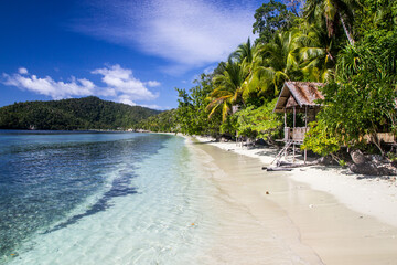 A simple hut in paradise palm trees on the white sand beach with crystal clear waters of the sea near the island Kri at Raja Ampat, West Papua