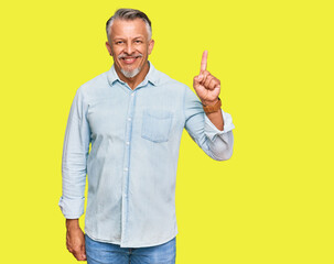 Middle age grey-haired man wearing casual clothes showing and pointing up with finger number one while smiling confident and happy.