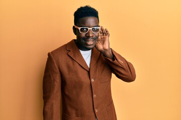 Obraz premium Handsome black man wearing elegant clothes and glasses smiling with hand over ear listening and hearing to rumor or gossip. deafness concept.